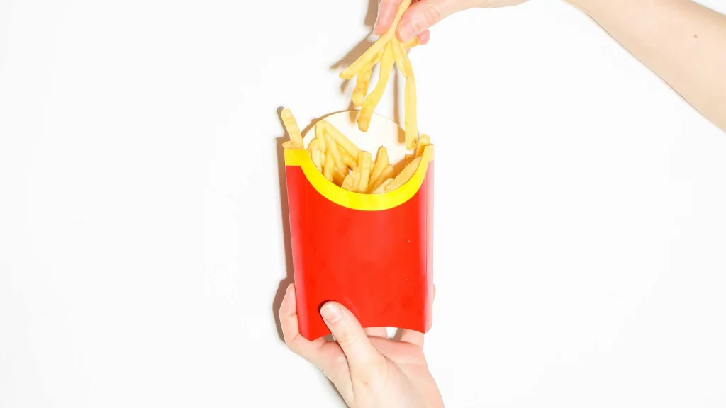 McDonalds Pommes Verpackung ohne das Logo drauf. Eine Hand hält die Verpackung, die andere nimmt Pommes heraus.